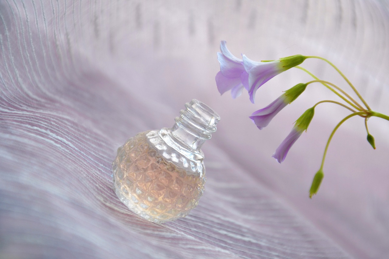 A small perfume bottle rests on a table beside a flower